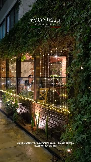 Fachada de Tarantella de noche: hiedra, ladrillo y una cortina de luces